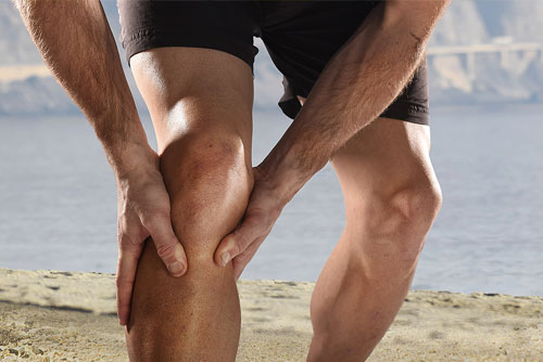 Jogger am Strand hält sich das Knie